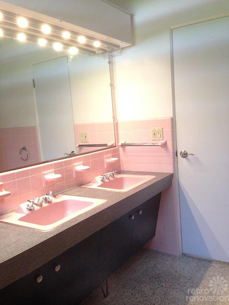 pink tile bathroom with black vanity and two sinks