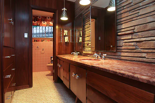 pink bathroom with dark wood paneling and stone wall